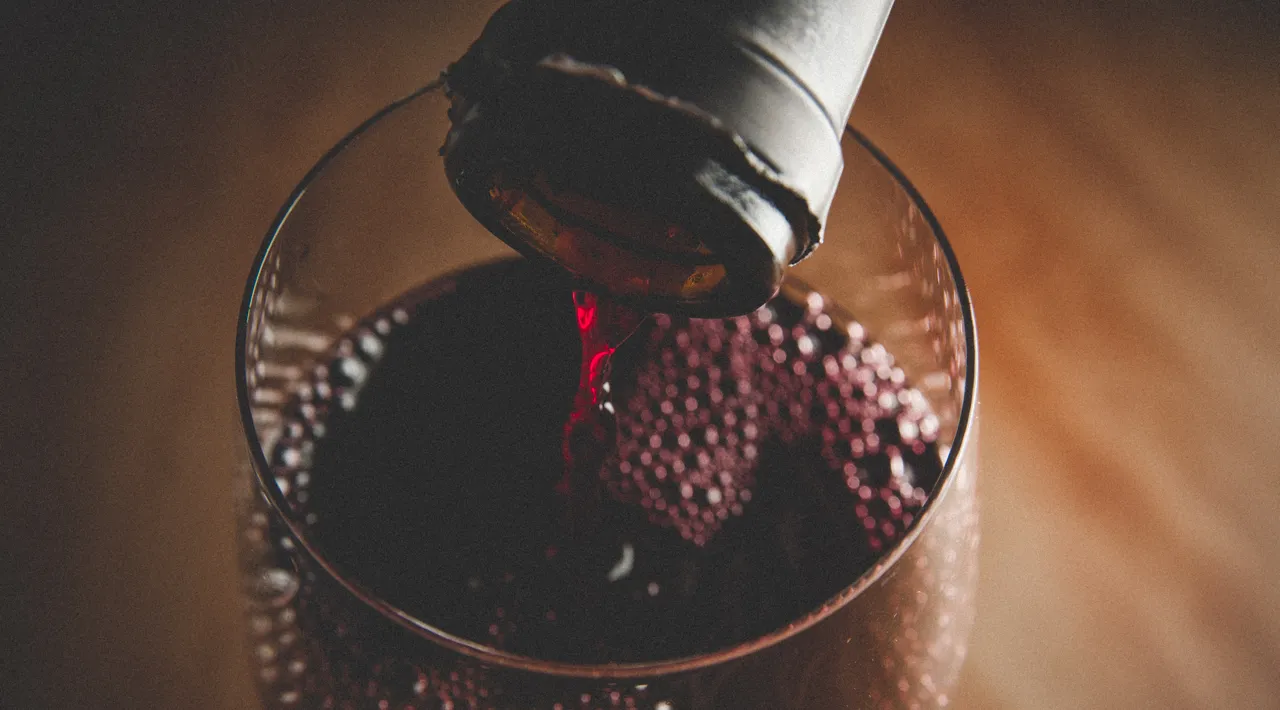 Wine glass being filled with red wine from a bottle