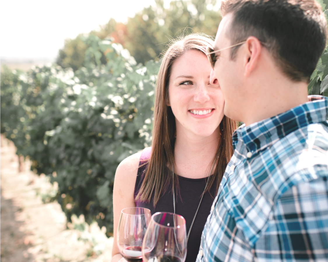 Two people with glasses of red wine talking in a vineyard