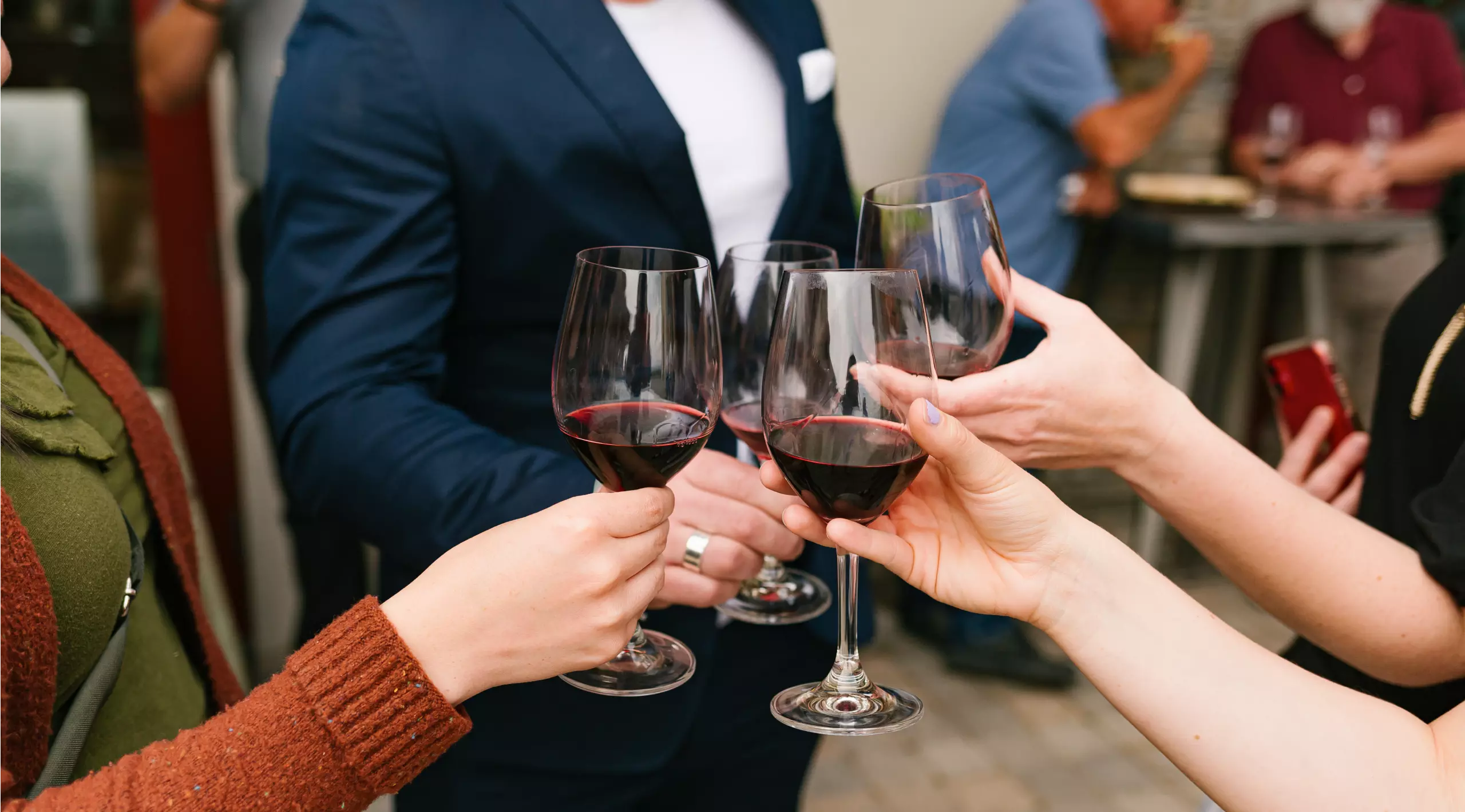 Hands holding up wine glasses full of red wine in a toast