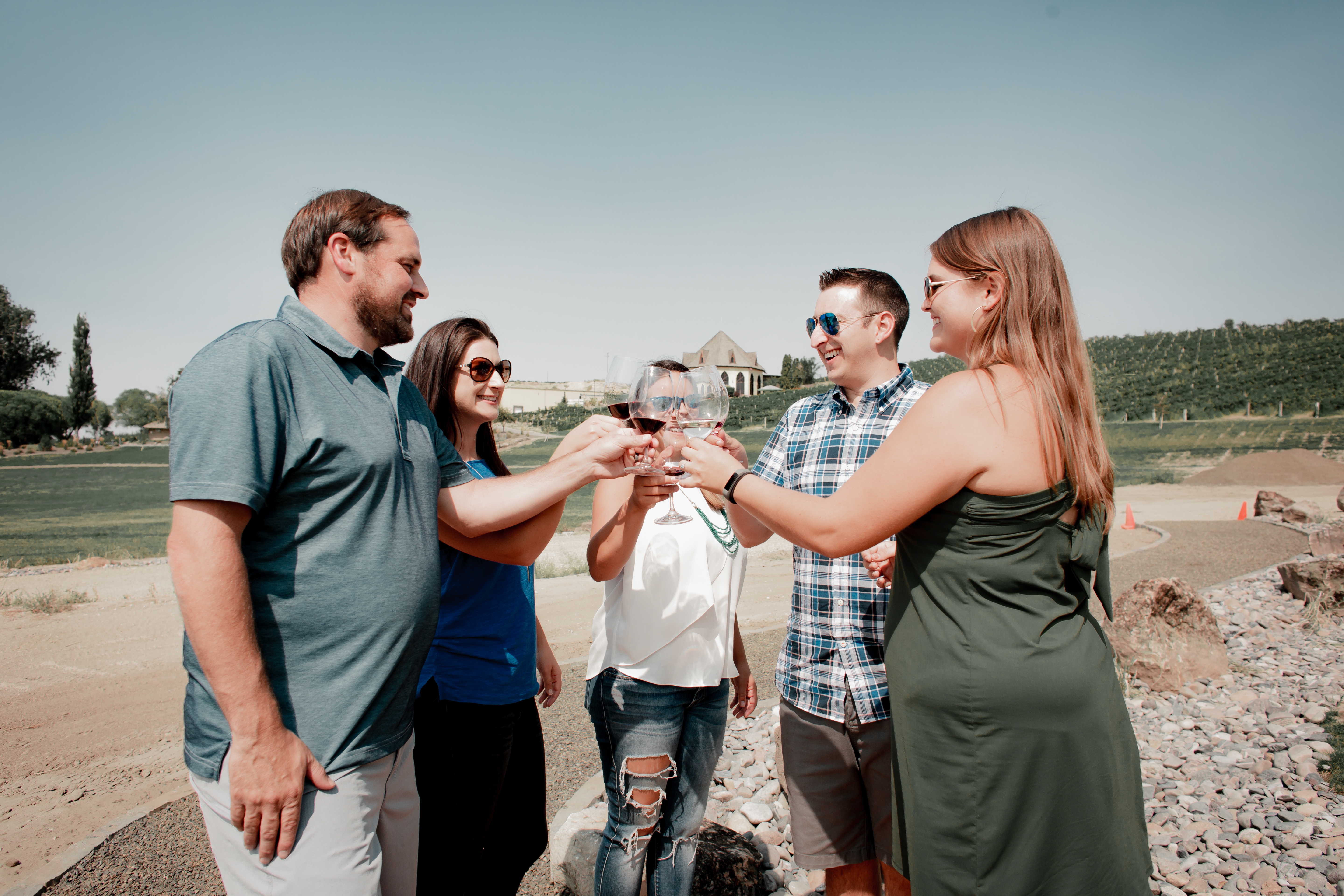 five people outdoors, holding wine glasses full of red wine up in a toast