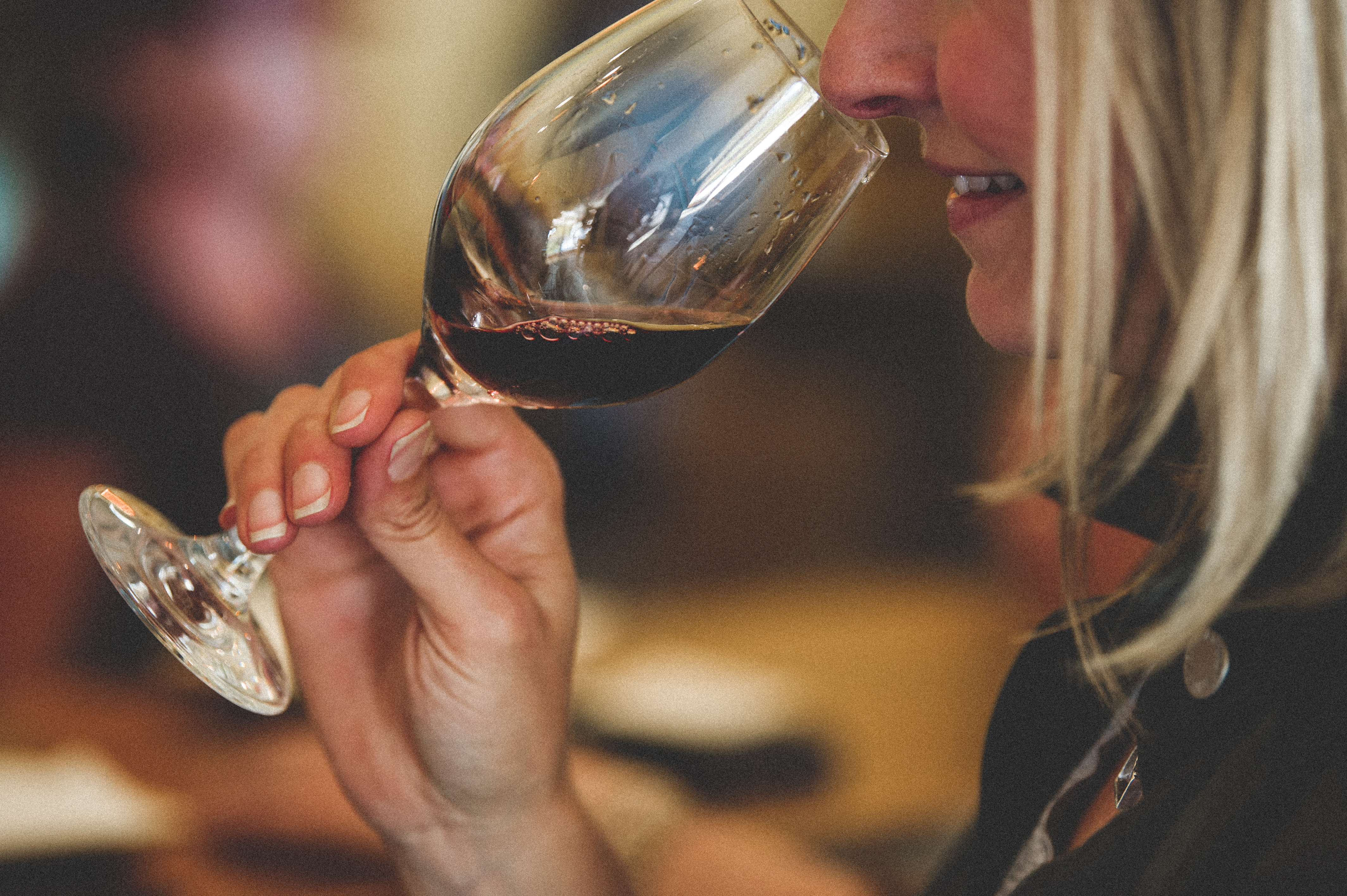 woman holding a wine glass full of red wine to her nose