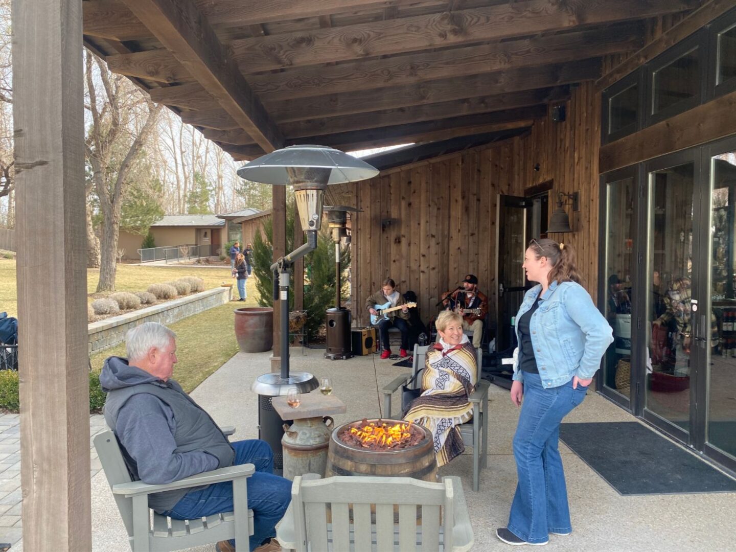 several people interacting in an outdoor space at a winery with chairs and a fire barrel